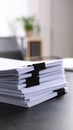 Stack of white paper documents held together with black binder clips on a dark desk Royalty Free Stock Photo
