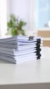 Stack of white paper documents held together with black binder clips on a white desk. Royalty Free Stock Photo