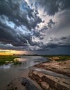 dramatic sky filled with dark clouds looms over a serene riverbank, reflecting the beauty and power of nature before a storm. Royalty Free Stock Photo