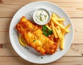 plate featuring crispy fried fish, golden fries, a side of tartar sauce, and garnished with parsley and lemon on a wooden table. Royalty Free Stock Photo