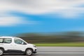 White compact van drives down the street, speed blurred background with free space for text, copy space.