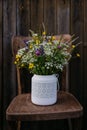 White vase with meadow flowers, herbs and grass, placed on a wooden chair. A colorful variety of summer wildflowers. Royalty Free Stock Photo