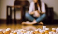 Blurry image of a distressed young woman sitting on the floor with focus on spilled prescription pills and medication bottles in