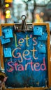 Close-up of a motivational message lets get started on colorful sticky notes held by a blue clipboard, suggesting