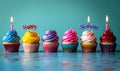 Colorful birthday cupcakes lined up with lit candles spelling Happy Birthday against a soft blue backdrop for festive Royalty Free Stock Photo