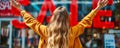 Excited young woman with arms raised in front of a store with a bright red SALE sign, depicting enthusiasm for shopping and Royalty Free Stock Photo