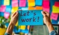 Hands holding a blue sticky note with the phrase lets work! amidst a chaotic background of colorful post-it notes and a Royalty Free Stock Photo