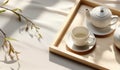 Top view of modern minimal beautiful white ceramic teapot teacup with saucer on brown straw mat wooden tray on cream tablecloth in Royalty Free Stock Photo