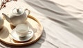 Top view of modern minimal beautiful white ceramic teapot teacup with saucer on brown straw mat wooden tray on cream tablecloth in Royalty Free Stock Photo