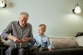 Generation. grandfather and grandson with gift box sitting on couch at home Royalty Free Stock Photo