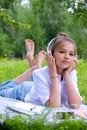 Teen girl lies listens to music in headphones on the grass in the park with books and notebooks Royalty Free Stock Photo