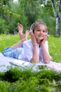 Teen girl lies listens to music in headphones on the grass in the park with books and notebooks Royalty Free Stock Photo