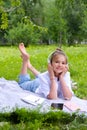 Teen girl lies listens to music in headphones on the grass in the park with books and notebooks Royalty Free Stock Photo