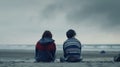 Generative AI Back view of two sad teenagers sitting on the sand of the beach and looking at horizon in a bad weat Royalty Free Stock Photo