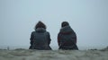 Generative AI Back view of two sad teenagers sitting on the sand of the beach and looking at horizon in a bad weat Royalty Free Stock Photo