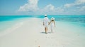Generative AI Happy couple in white clothing and with hats walks down a tropical beach with turquoise sea in the M Royalty Free Stock Photo