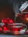 Generative AI Hot tea is pouring from glass teapot into cup. Hibiscus red tea in glass cup close-up view business Royalty Free Stock Photo