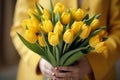 Generative AI International Women's Day. A woman in a yellow raincoat holds a lush bouquet of yellow tulips