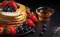 Stack of golden pancakes with fresh blueberries and strawberries on the side, accompanied by a bowl of maple syrup on a dark Royalty Free Stock Photo