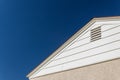 Generic house view of side and roof edge, stucco and vinyl with attic ventilation set against a deep blue sky