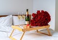 Celebrating Saint Valentine`s Day with bouquet of red roses, glass of champagne and croissants on tray on bed. Romantic surprise Royalty Free Stock Photo