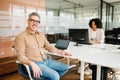 A genial senior business leader sits at an office table with a laptop