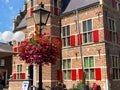 View on brick facade with red shutters of former dutch medieval town hall beyond flowers