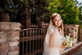 gentle and beautiful bride in a veil with a bouquet of flowers at the fence.
