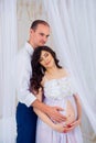 Gentle beautiful pregnant couple near tulle curtains