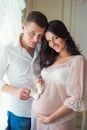 Gentle beautiful pregnant couple near tulle curtains