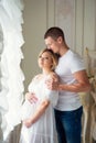 Gentle beautiful pregnant couple near tulle curtains