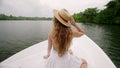 Woman in straw hat enjoys serene river cruise, seated at boat bow, amidst lush tropical greenery. Gentle breeze in hair