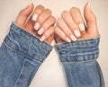 Gentle camouflage gel polish on square nails with a French design. Hands with a professional manicure in a denim jacket.