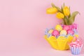 Gentle elegant soft pastel easter decoration - painted eggs, yellow tulips, cupcake on pink background, copy space.