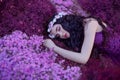 A gentle and graceful girl sleeps on a magical purple flower field, a dreaming beauty with long dark hair and a pink