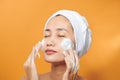 Gentle half-naked woman wrapped in towel washing her face with foaming cleanser isolated over orange background Royalty Free Stock Photo