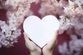 Gentle hands hold an ethereal, empty paper heart, set against a backdrop of vibrant flowers