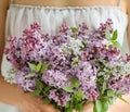 Gentle hands of a woman in a white dress cradle a lush bouquet of lilac
