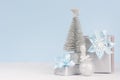 Gentle home decor for New Year celebration - silver gift boxes and small sparkles fir, ball on white wood table and soft blue. Royalty Free Stock Photo