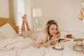 Gentle image of cute fair-skinned young girl with great appetite looks at cake, lying on bed. Royalty Free Stock Photo