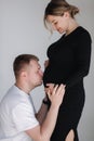 Gentle man kissing his pregnant wife belly. Man in white shirt and female in black dress Royalty Free Stock Photo