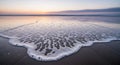 Gentle ocean wave with intricate foam patterns washes onto a sandy beach at sunrise Royalty Free Stock Photo