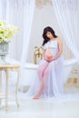 Gentle pregnancy. Beautiful pregnant in light white dress with orchids