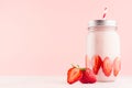 Gentle strawberry yogurt in jar decorated sliced ripe berry with silver lid and red striped straw on soft pastel pink background. Royalty Free Stock Photo