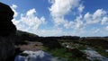 A gentle upward motion pan over rockpool with seaweed, to reveal lapping waves and distant headland.