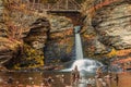 Gentle waterfall flows under footbridge to calm water adorned with cairns Royalty Free Stock Photo