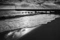 Gentle waves and foam on a sandy beach with groins and a pier late in the afternoon as the sun rays break through the clouds