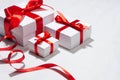 Gentle white gift boxes with red silk bow on white wood table as festive anniversary background, closeup.