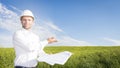 Geodesist with drawings on ground for building building. Builder in white helmet and project documentation on green meadow Royalty Free Stock Photo