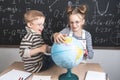 Geography lesson: A boy and a girl are sitting on a desk and studying the globe on the background of a school board. Royalty Free Stock Photo